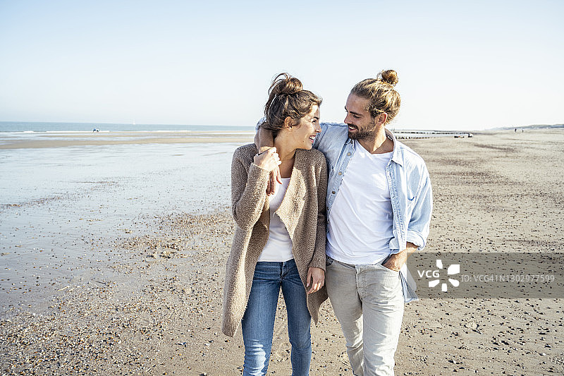 周末在海滩上散步时，一对年轻的情侣微笑着看着对方图片素材