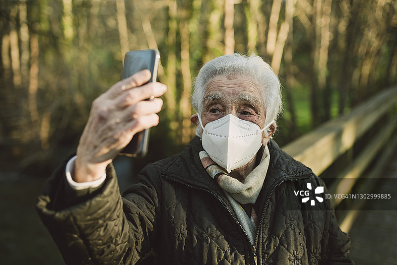 年长女性戴着防护口罩，在冬天用智能手机自拍图片素材
