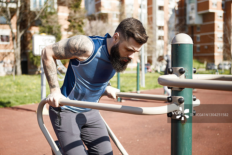 年轻的肌肉男在公园里锻炼，三头肌和手臂图片素材