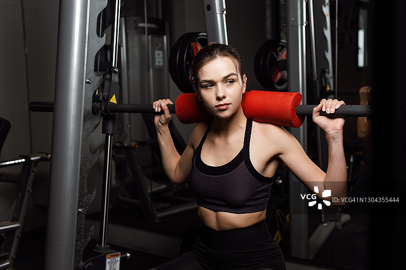 运动女孩在健身房用杠铃做下蹲。图片素材