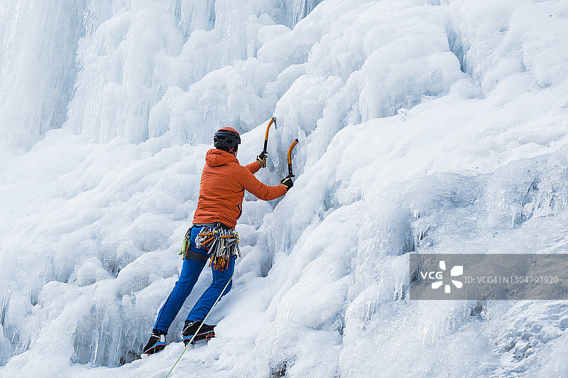一只雄性冰攀登者带着冰斧和冰爪爬上陡峭的冰墙图片素材