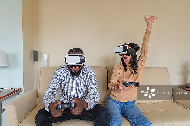 兴奋的多民族年轻夫妇正在用VR眼镜和手柄玩视频游戏，度过美好的时光。图片素材