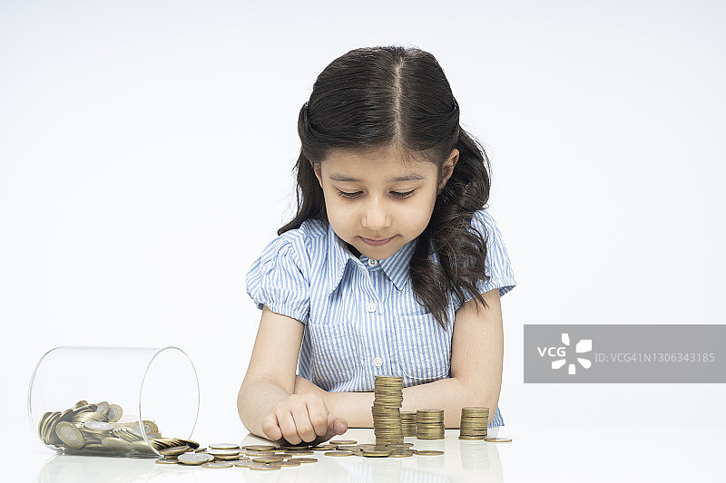 肖像的印度可爱的小女孩与玻璃罐的硬币坐孤立在白色的背景:股票照片图片素材