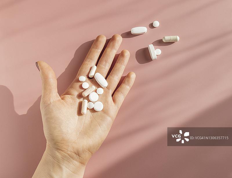 粉红色背景下，一个匿名者的手拿着不同的药片和胶囊图片素材