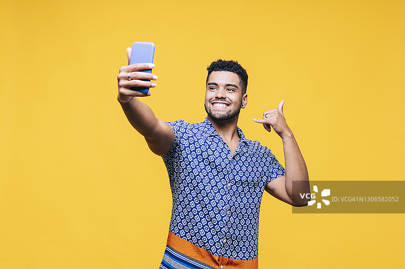 黄色背景下，微笑的男人打着手势自拍手机图片素材