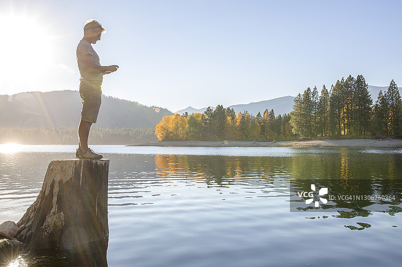 清晨，一个人站在湖边的树桩上图片素材