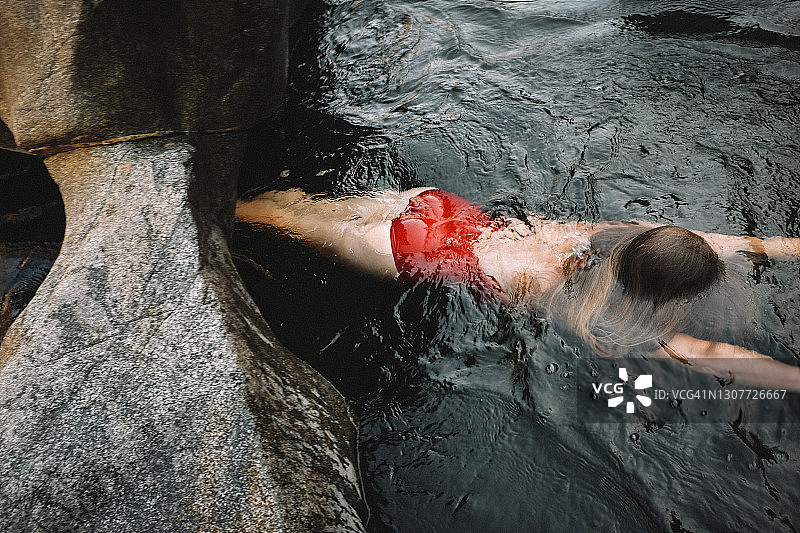 穿着红色游泳衣的女人漂浮在黑水里图片素材