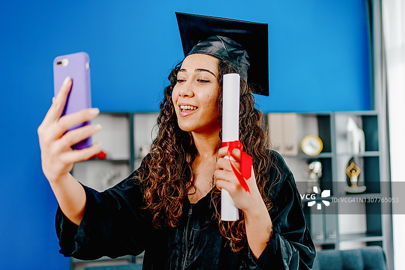 女孩穿着毕业礼服和帽子在视频电话问候她的亲戚或朋友图片素材