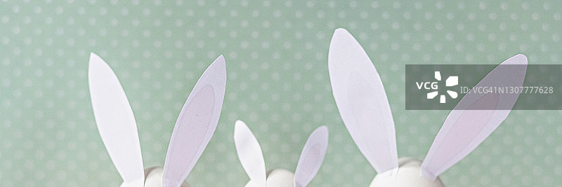 白色的鸡蛋，兔子耳朵和尾巴在床上花的背景。一个家庭。复活节节日快乐概念。横幅图片素材