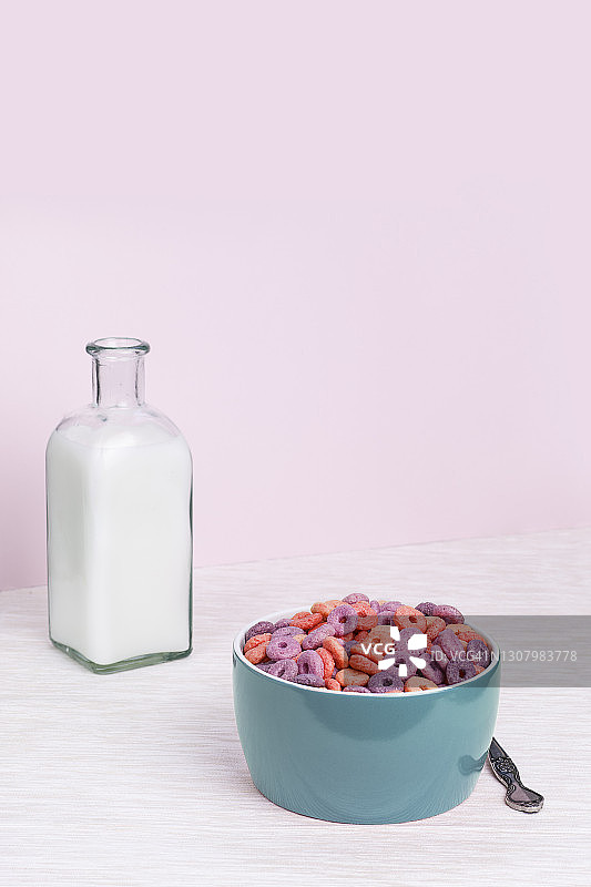 蓝色的环形麦片碗，一个方形的玻璃瓶，里面装着牛奶，背景是粉红色和白色图片素材