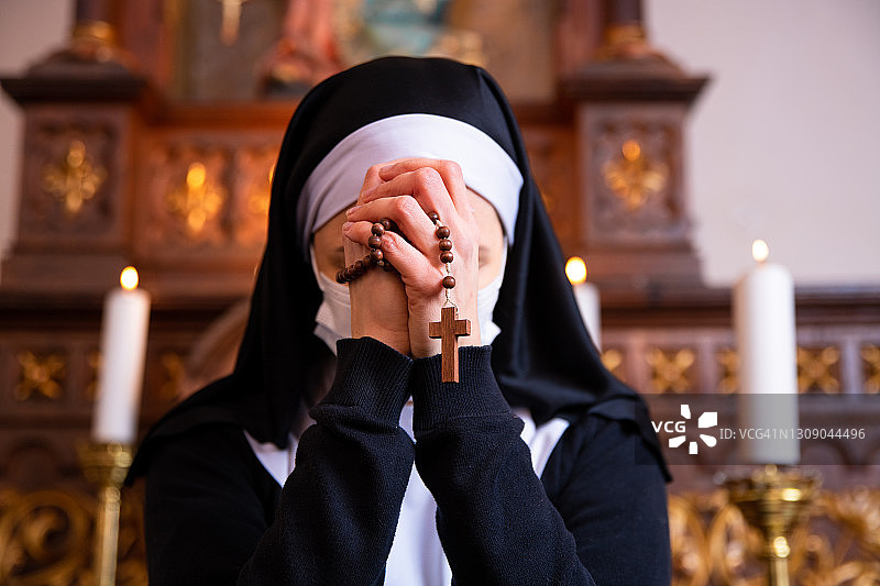 低头祈祷的修女靠近拿着念珠的手。图片素材