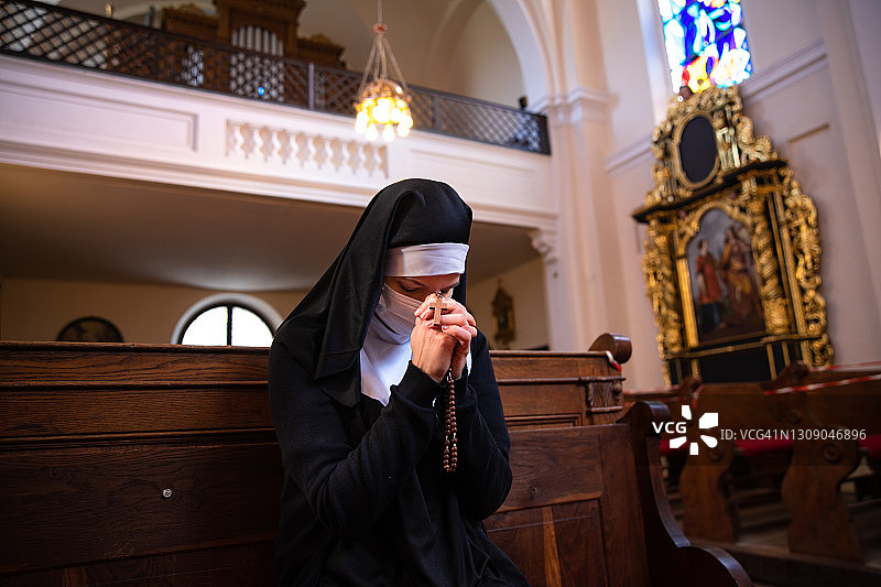 在教堂里，一名修女戴着保护面罩，手拿念珠，低头祈祷。图片素材