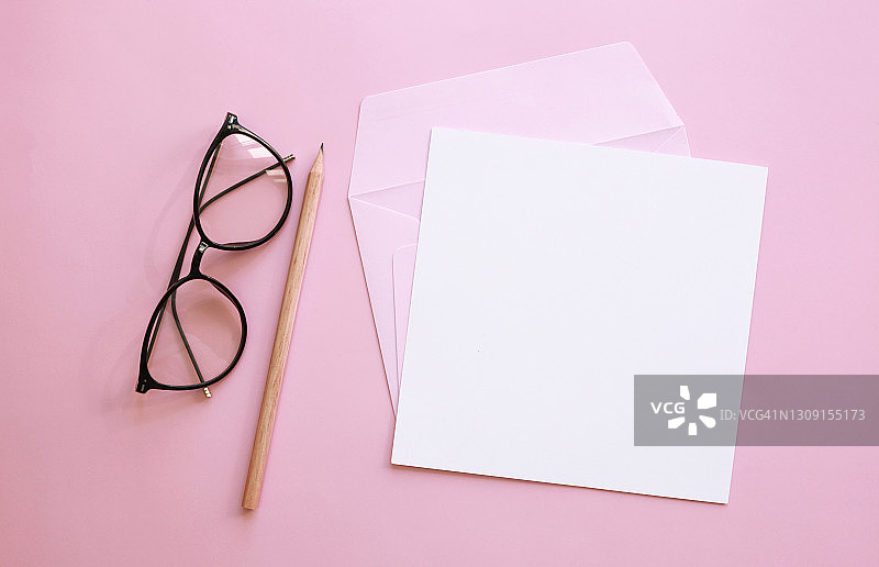 办公或学习用品。眼镜，粉红色信封上的空白白纸卡，粉红色背景上的铅笔。图片素材