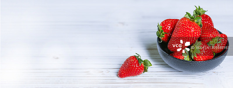 白桌子上黑碗里装着新鲜的红草莓。横幅照片。图片素材