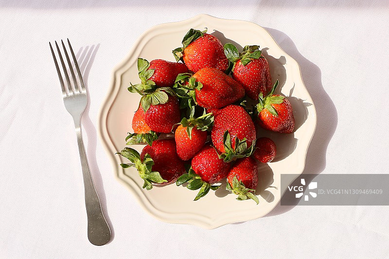 白色桌布上，白色陶瓷盘子上放着草莓，阳光明媚的一天图片素材