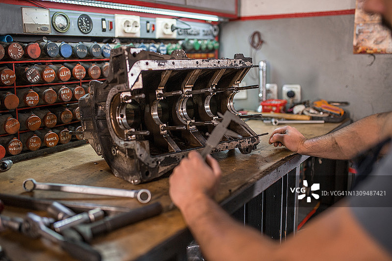 一个年轻的机修工在汽车修理厂用工具修理旧汽车引擎图片素材