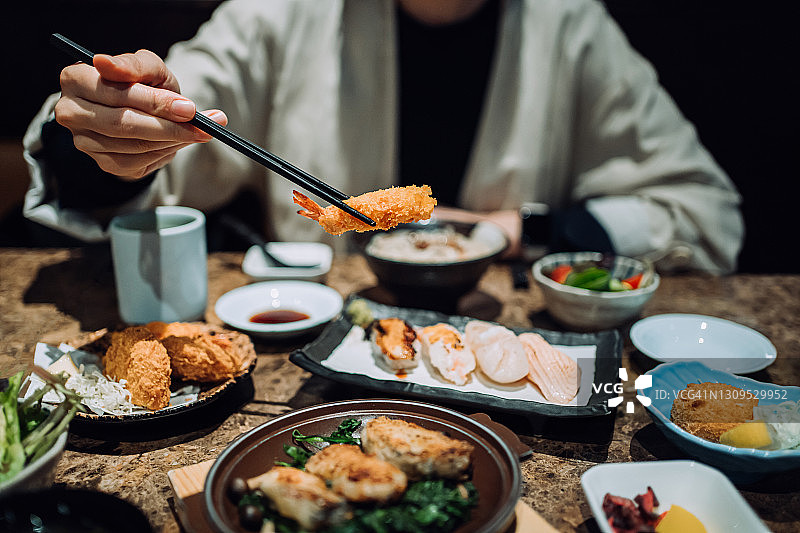 近距离的年轻亚洲女子享受精致的日式料理什锦寿司，海鲜天妇罗和烤生蚝新鲜在餐厅的餐桌上。亚洲菜肴和食物。外出就餐的生活方式图片素材