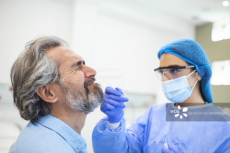 医护人员使用防护设备对老人进行冠状病毒拭子。鼻拭子检测Covid-19。图片素材
