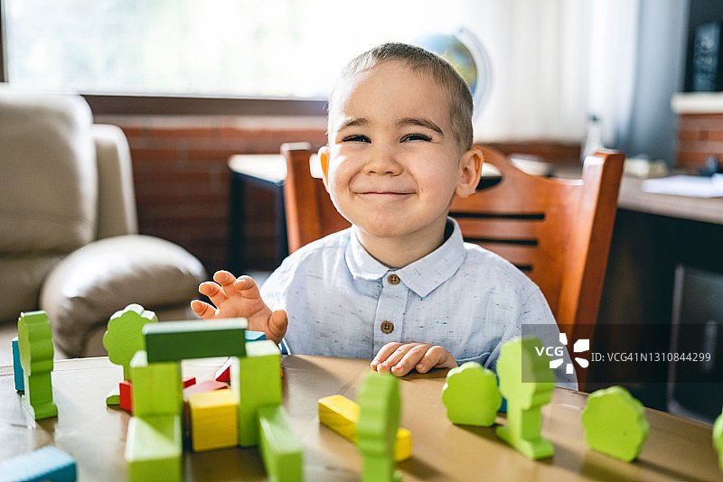 快乐的蹒跚学步的小男孩在家里玩五颜六色的玩具积木图片素材