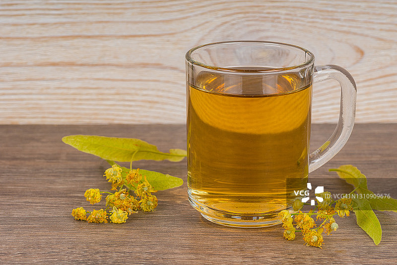 草本茶在透明玻璃杯和新鲜的椴树花在木桌上图片素材