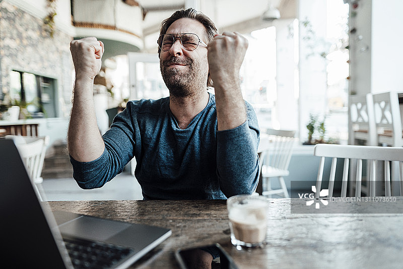 快乐的男企业家在咖啡店里用笔记本电脑做拳头图片素材