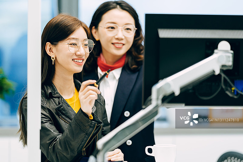 两位职业亚洲女商人在电脑前努力工作在办公室。图片素材