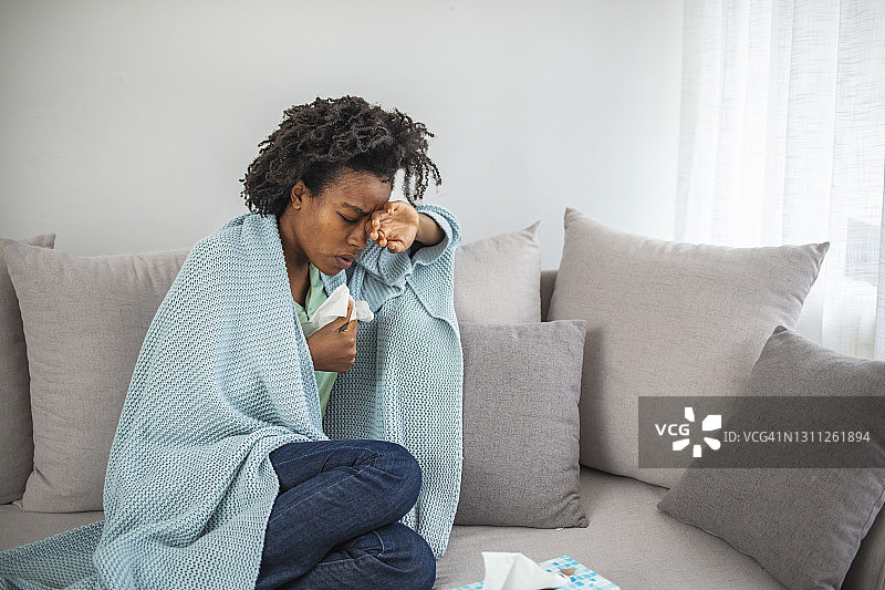 忧心忡忡的非裔美国妇女在生病时坐在家里。图片素材