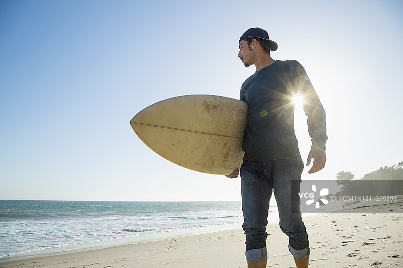 日落时分，一个年轻人带着冲浪板站在海滩上图片素材