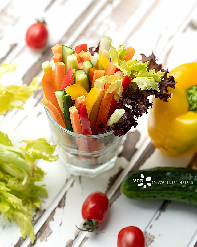 维他命沙拉，彩色的新鲜蔬菜条放在玻璃里。早餐小吃西红柿，黄瓜，甜椒和生菜在乡村的桌子上。健康饮食，素食和纯素餐。软焦点图片素材