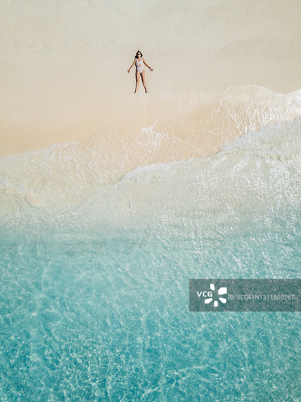 年轻的成年女子躺在天堂般的海滩上，背靠马尔代夫碧绿的海水图片素材