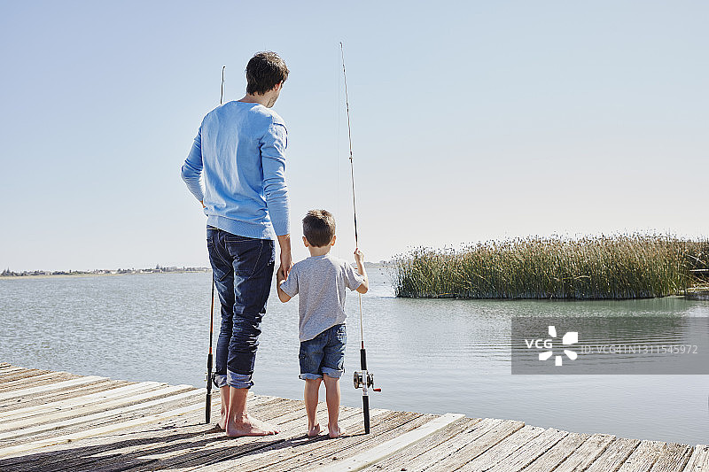 父亲和儿子手牵着手站在码头上钓鱼竿图片素材