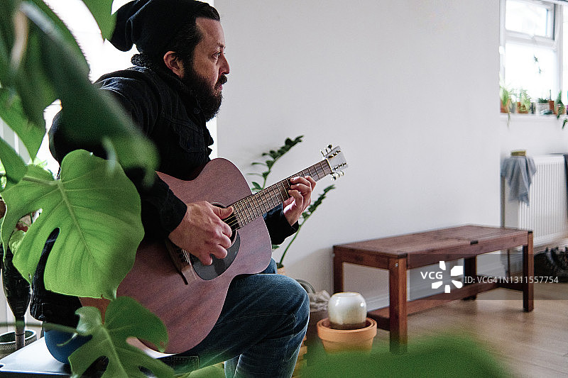 成熟的男人坐在家里弹吉他图片素材