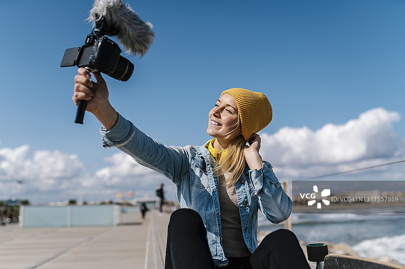 快乐的女人在牛仔衬衫通过摄像头在周末录制视频图片素材