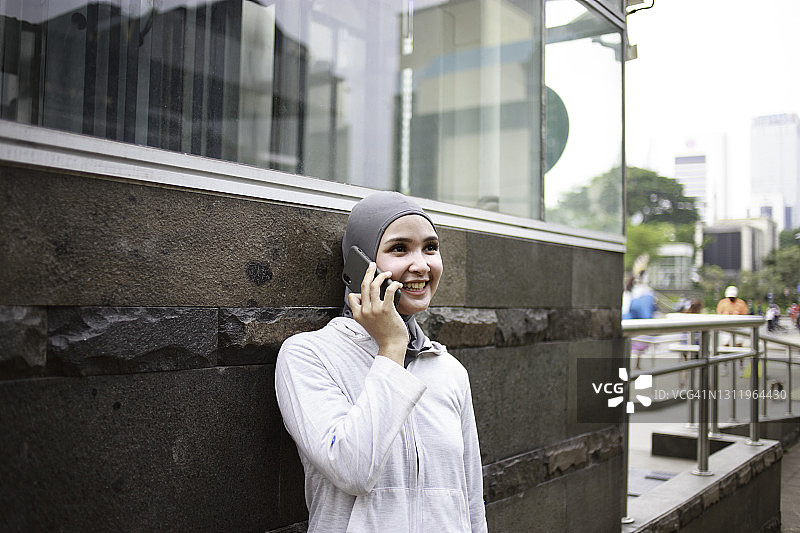 年轻的亚洲妇女戴着头巾微笑着，使用手机，穿着运动服图片素材