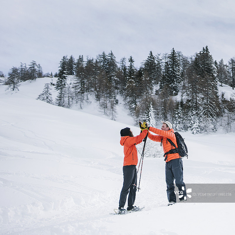 早上，穿着雪鞋的朋友们在雪坡上击掌图片素材