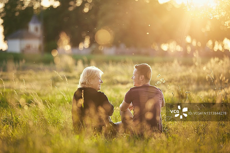 日落时分，母亲和儿子坐在草地上图片素材