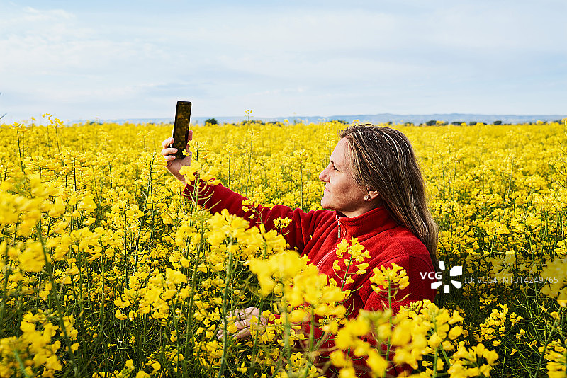 快乐的女人在盛开的黄色油菜花地里为她的社交媒体拍照图片素材
