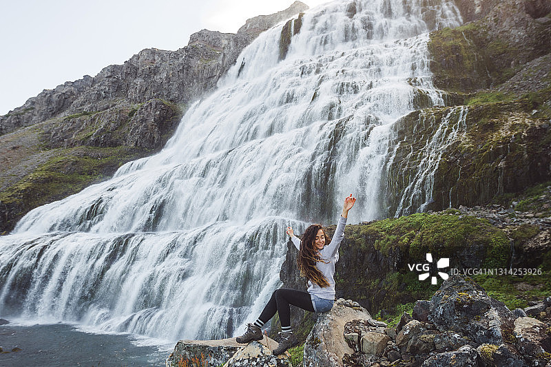 年轻快乐的女人欣赏Dynjandi瀑布。西峡湾著名的冰岛瀑布令人叹为观止图片素材