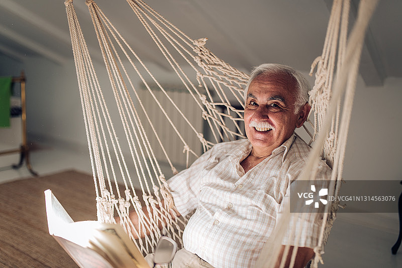 一个快乐的老人的肖像阅读和放松在吊床上图片素材
