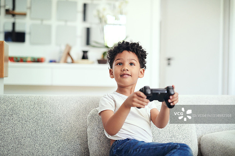 一个小男孩坐在沙发上，手里拿着游戏控制器图片素材