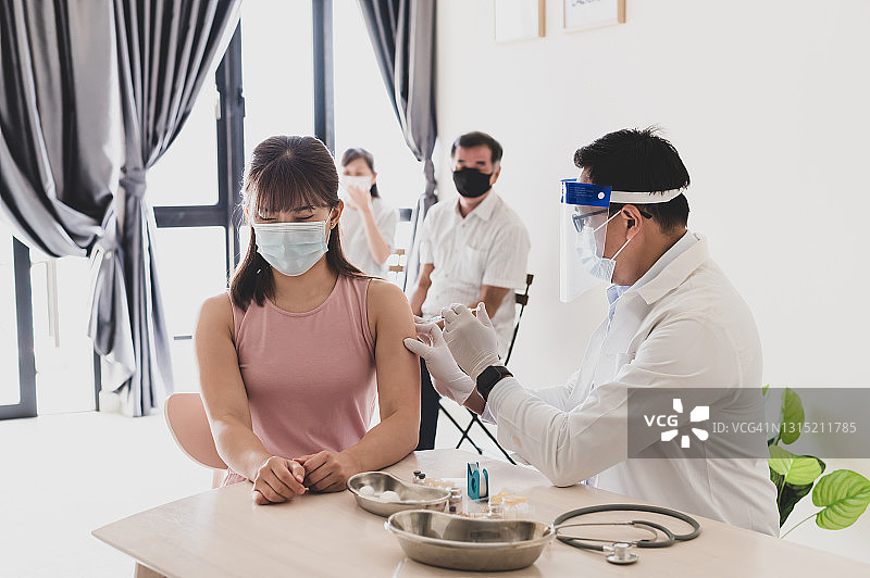 男医生戴防护口罩，戴手术手套，手持Covid-19疫苗注射器，在医学实验室为一名年轻的亚洲华裔女性进行注射。图片素材