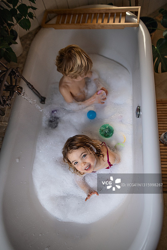 俯视图的小孩在浴室在家里，享受泡泡浴的乐趣。图片素材