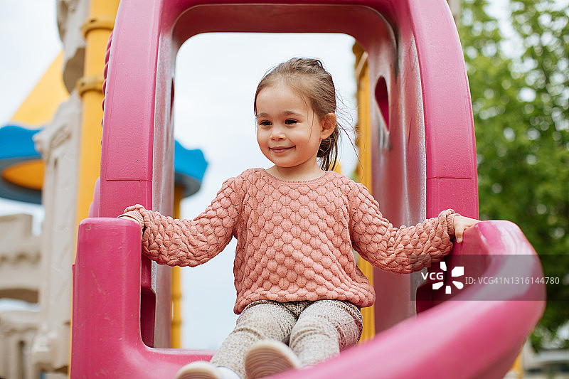 一个2-3岁的女孩滑下滑梯是非常快乐，积极的情绪图片素材