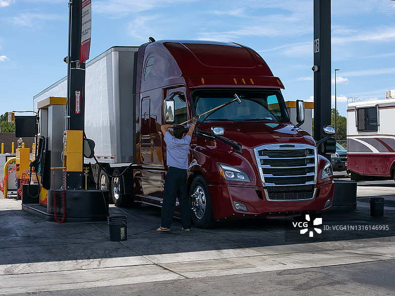 一位卡车司机在卡车停靠站清洗卡车驾驶室的挡风玻璃。图片素材