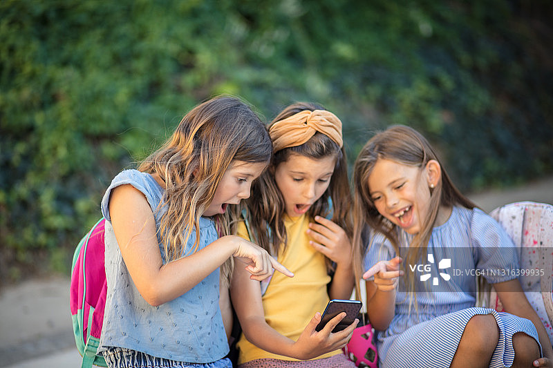三个小女孩在大自然中使用智能手机。图片素材