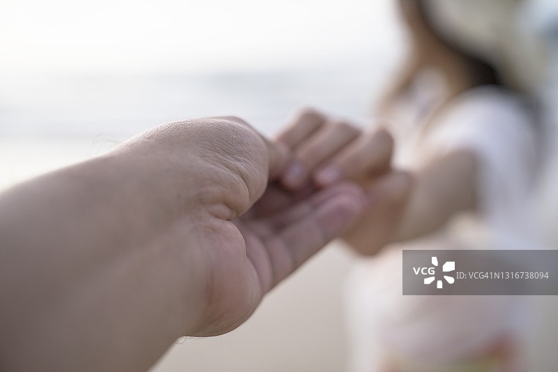 年轻的情侣手牵着手，男友远景跟着女友去海滩。图片素材
