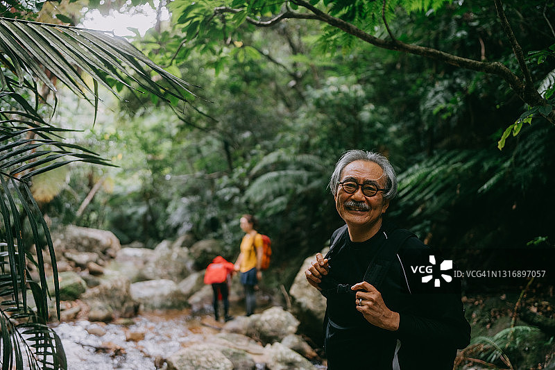 老人享受徒步穿越热带雨林的河流，冲绳，日本图片素材