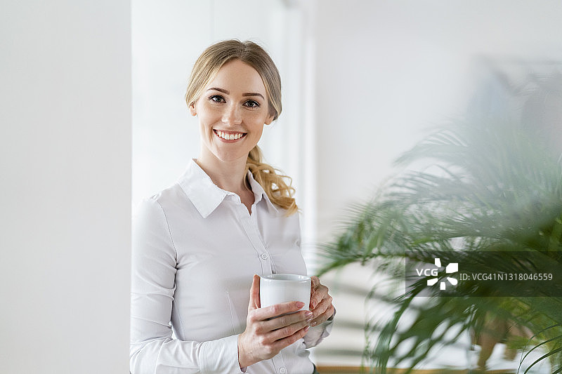 微笑美丽的职业女性拿着咖啡杯在办公室图片素材