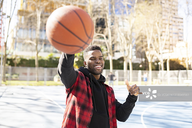 在阳光明媚的日子里，一个快乐的男人在打篮球时展示了沙卡的标志图片素材
