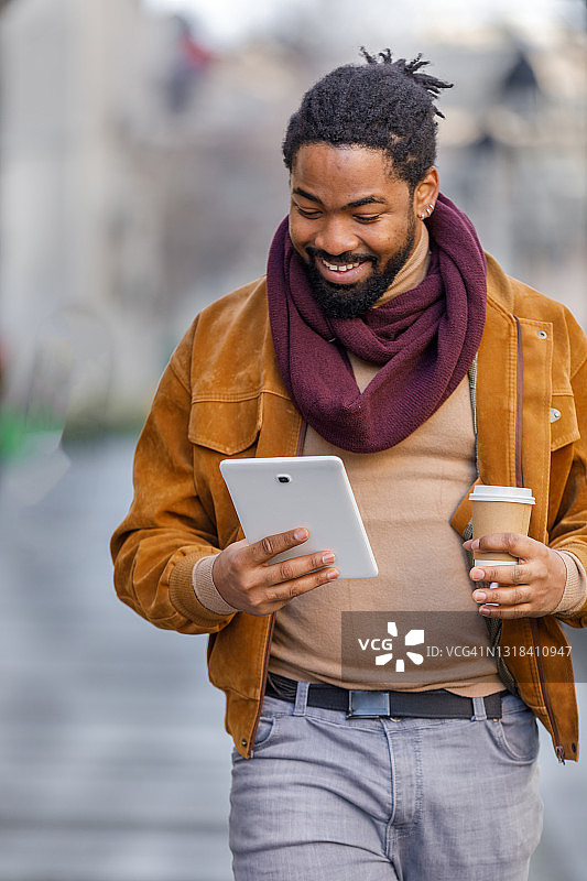 年轻帅气的非洲裔男子带着平板电脑在城市里散步，并享受一杯咖啡。图片素材